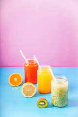freshly squeezed fruit juice, smoothies yellow orange green lemon apple orange kiwi on bright blue and pink background Copy space.