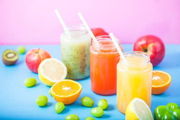 freshly squeezed fruit juice, smoothies yellow orange green blue banana lemon apple orange kiwi grape strawberry on bright blue and pink background Close up.