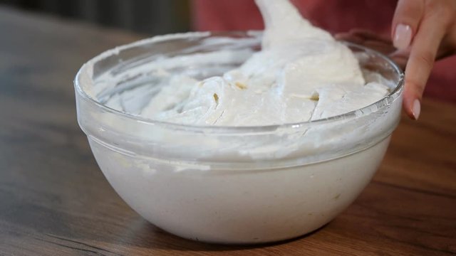 Chef with spatula stirring macaron batter or cream in bowl at pastry shop.