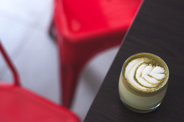 Top view of hot matcha coffee mocaccino cappuccino latte art in ceramic cup on wooden plate and red chair. Matcha cup top view on old table. Tea cup in coffee shop. Beautiful green foam, glass cups,