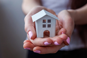 Female hands holding small miniature white toy house. Mortgage property insurance dream moving home and real estate concept