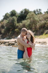 Romantic couple of man and woman hugging in the clear sea water near the beach in Greece. Sunny summer day