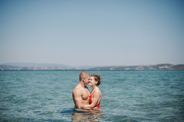 Happy caucasian couple of man and woman kissing while swimming in the clear blue sea water. Sunny summer day. Vacation in Greece
