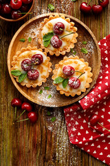 Mini Tarts with fresh cherries and vanilla custard and caramel, delicious dessert on a wooden table, top view