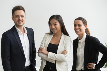 Millennial smiling multi-ethnic professional office employees looking at camera, asian and caucasian creative group of three happy business people in suits together, successful diverse team portrait