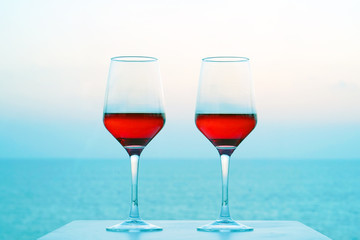 Two glasses of red wine on a background of sea horizon morning. Two glasses of red wine with blue sea in background. Two Glasses of Red Wine Standing on Table at the hotel balcony.