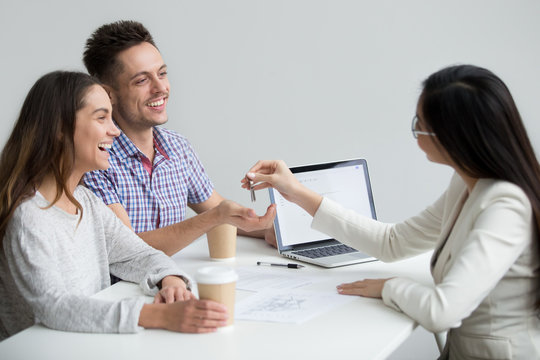 Excited millennial couple get keys become first time home owners make new house purchase deal with realtor, smiling customers or renters happy to buy rent real estate, property ownership concept