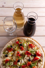 Top view focaccia with cheese, tomato and olives and two pitchers with red and white wine