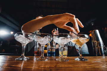 Barman decorates glasses for an alcoholic cocktail at bar counter.