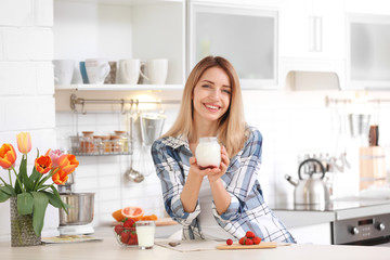 Young woman with tasty yogurt at table in kitchen