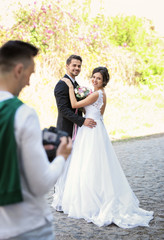 Naklejka premium Wedding couple and professional photographer with camera, outdoors