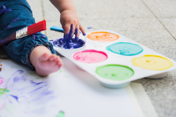 White toddler foot on paint covered paper and dipping hand into purple paint.