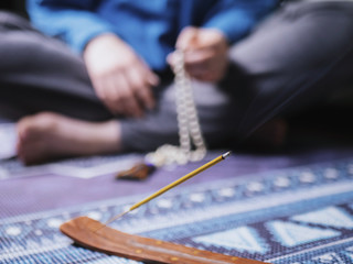 Concentrated woman praying with wooden rosary mala beads. Close up, focus on incense stick