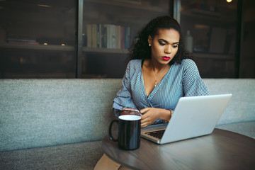 Young businesswoman using smartphone while looking at laptop