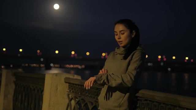 sports girl rests after jogging in the night city. athlete heart rate monitors on smart watches