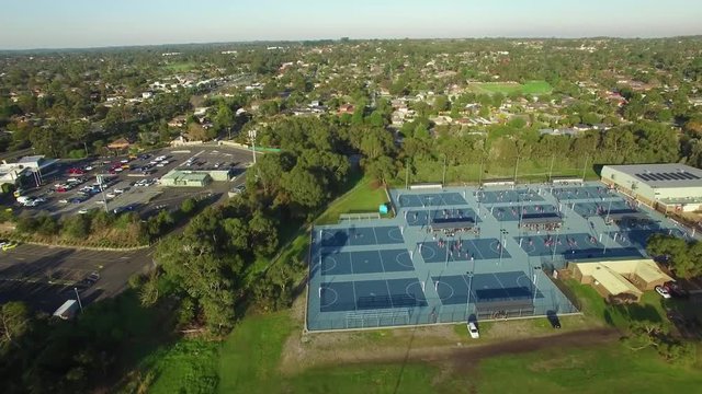 Forward flight over sports oval and people playing on netball courts in urban area