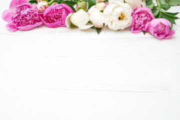 White and pink peonies on white wooden table. Holiday background, copy space, top view