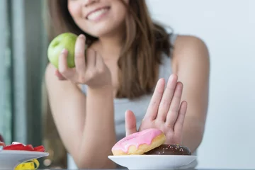 Foto op Plexiglas Woman on dieting for good health concept. Close up female using hand push out her favourite donut and choose green apple and vegetables for good health. © Pormezz