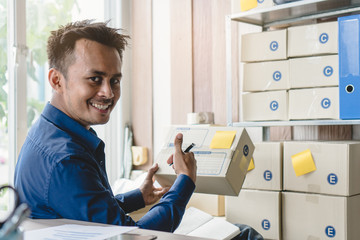 Fototapeta premium Concept modern new asian entrepreneur. E-commerce business owner calling to supplier to confirm order and reviewing checklist of customer address before sent box of product by parcel post.
