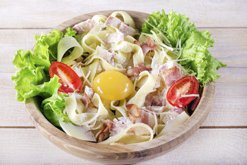 Pasta Carbonara with bacon on a wooden plate, close-up.