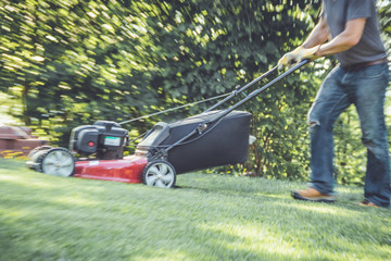 Red lawn mower cutting grass being pushed - intentional motion blur to create effect