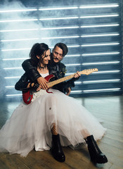 Wedding in the style of rock. Rocker or Biker wedding. Guys with stylish leather jackets. It's a rock'n'roll baby Sweet couple in a photo studio. Steep shooting with electric guitar and smoke.