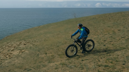 Fototapeta na wymiar Fat bike also called fatbike or fat-tire bike in summer driving through the hills. The guy is riding a bike along the sand and grass high in the mountains. He performs some tricks and runs dangerously