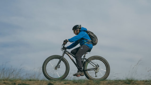 Fat bike also called fatbike or fat-tire bike in summer driving through the hills. The guy is riding a bike along the sand and grass high in the mountains. He performs some tricks and runs dangerously