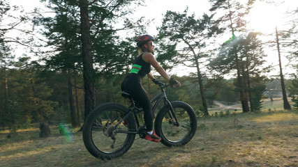 Fototapeta premium Fat bike zwany także fatbike lub fat-tire bike latem podczas jazdy po lesie. Piękna dziewczyna i jej rower w lesie. Toczy rower i pozuje do operatora.