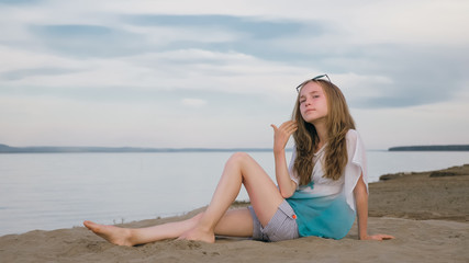 Fototapeta na wymiar One beautiful teenage girl with brown hair outside on a beautiful summer day. The woman is sitting on the beach. The sun was gone in the sunset.