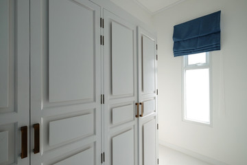 White clothes closet in room with window and navy blue color sun blind keep opened