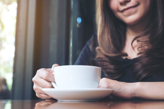 Closeup image of a beautiful woman holding and drinking hot coffee in cafe
