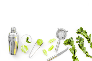 Process of making mojito concept. Ingredients and crockery. Slices of lime, mint, glass with ice cubes, shaker, strainer on white background top view copy space