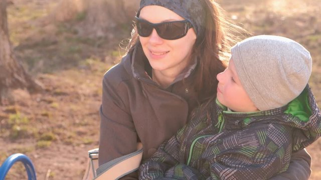 Mom and son look around and talk sitting on a bench in the Park in the spring.