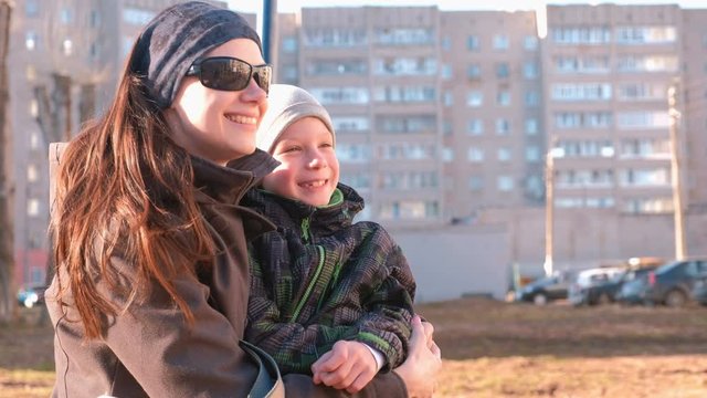 Mom and son look around, laugh and talk sitting on a bench in the Park in the spring.
