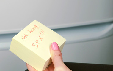 Block of yellow sticker paper sheet with words not having sex in woman's hand.