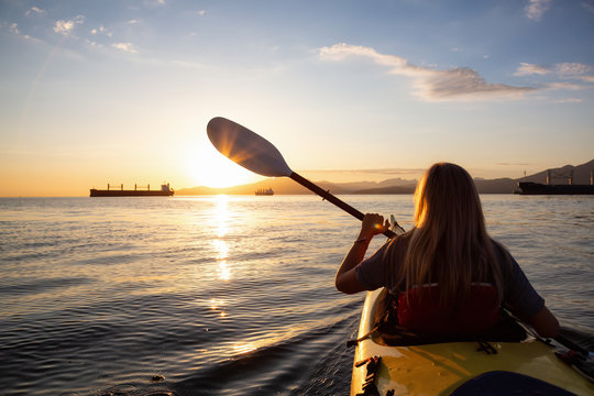 Woman on a kayak is paddeling in the ocean during a vibrant sunset. Taken in Vancouver, British Columbia, Canada. Concept: adventure, holiday, lifestyle, sport, recreation, activity, vacation