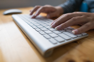 Close up image of female hands typing text on a wireless keyboard. Business woman working at the office. On wooden table