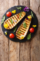 Portion of grilled eggplant and tomato with herbs and edible flowers close-up. Vertical top view