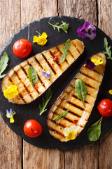 Summer appetizer from grilled eggplants and tomatoes with herbs and edible flowers close-up. Vertical top view