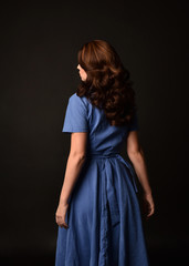 3/4 portrait of brunette lady wearing blue dress, facing away from camera. posed on black studio background.