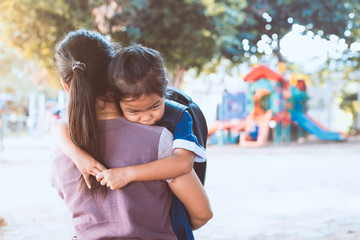 Fototapeta na wymiar Back to school. Cute asian pupil girl with backpack hugging her mother with sadness in the playground before go to classroom in the school.