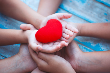 Red heart in child and parent hands with love and harmony. Family holding red heart together