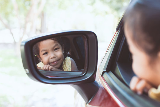 Cute Asian Little Child Girl Smiling And Having Fun To  Travel By Car And Looking At Side View Mirror In The Car