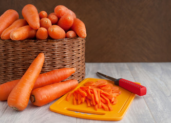 Harvest carrots in a large box. A lot of carrots in a wicker basket on a wooden background. Preparation of dishes from carrots. Sliced vegetables on a cutting board.