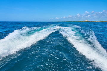 Trail on water surface behind of fast moving motor catamaran in the Caribbean Sea Cancun Mexico. Summer sunny day, blue sky with clouds.