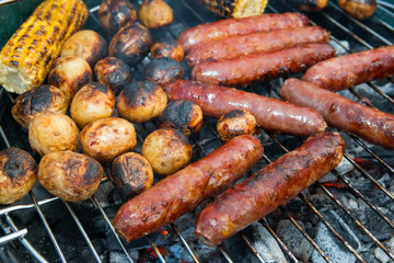 Baked potatoes, corn and sausages on a barbecue grill