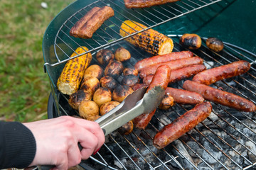 Baked potatoes, corn and sausages on a barbecue grill