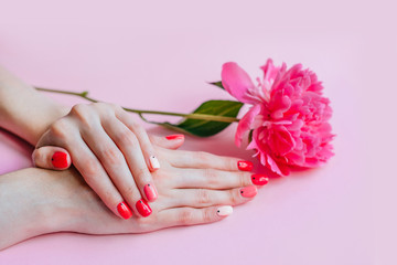 Creative bright trendy summer manicure with nails of different color. Female hands with art nail design on pink background and fuchsia peony flower.