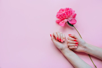 Creative bright trendy summer manicure with nails of different color. Female hands with art nail design on pink background and fuchsia peony flower.